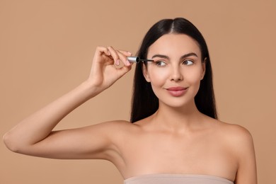 Photo of Beautiful woman applying serum onto her eyelashes on beige background. Cosmetic product