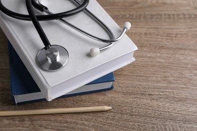 Student textbooks, pencil and stethoscope on wooden table, closeup. Medical education