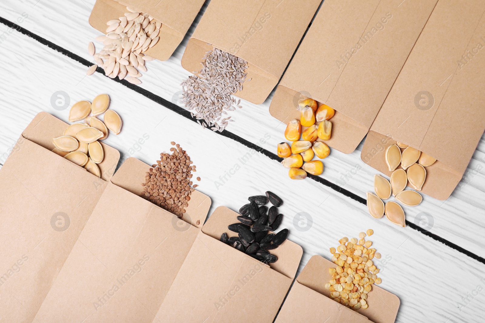 Photo of Many different vegetable seeds on white wooden table, flat lay