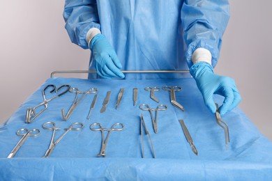 Doctor holding medical forceps near table with different surgical instruments on light background, closeup