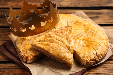 Photo of Traditional galette des Rois with paper crown on wooden table, closeup