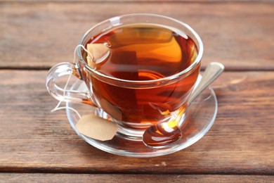 Photo of Brewing aromatic tea. Cup with teabag and spoon on wooden table