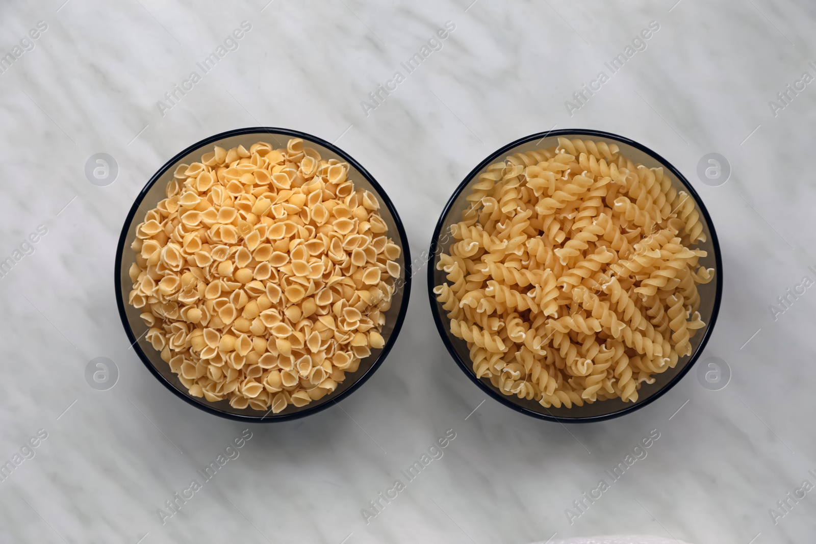 Photo of Different types of pasta on white marble table, flat lay