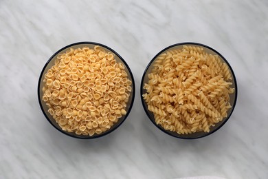 Different types of pasta on white marble table, flat lay