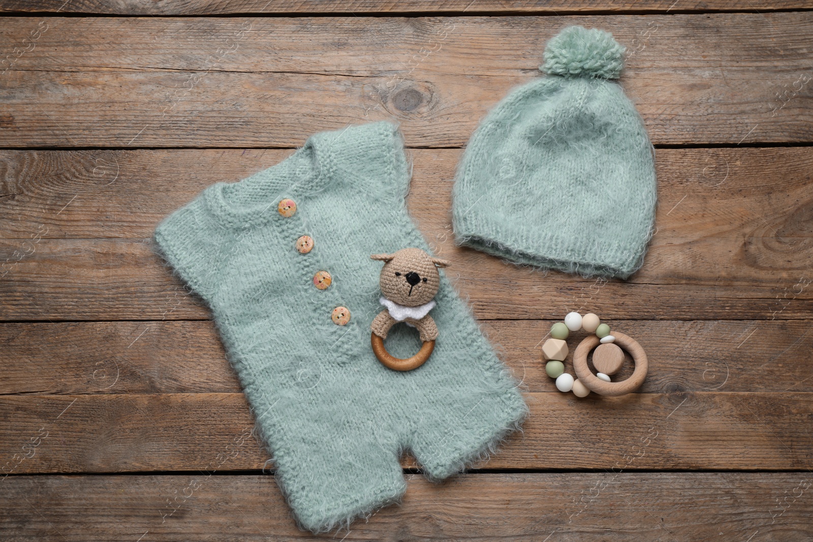 Photo of Baby toys, knitted romper and hat on wooden background, flat lay