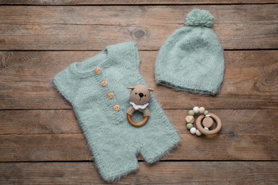 Photo of Baby toys, knitted romper and hat on wooden background, flat lay
