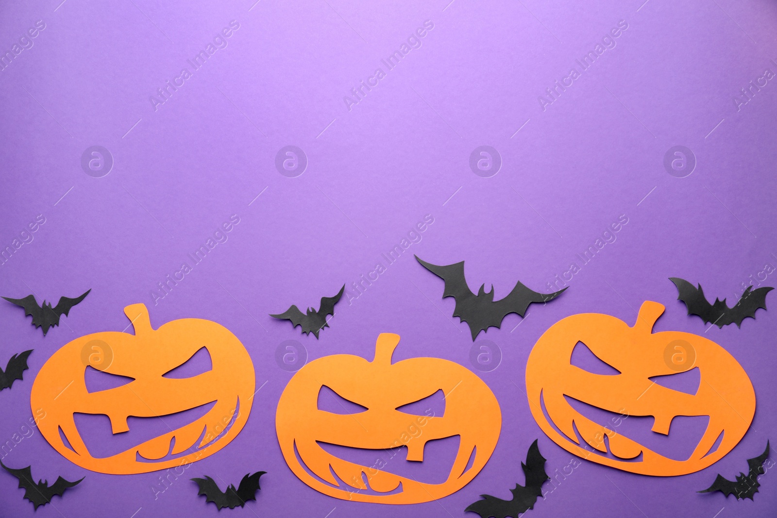 Photo of Flat lay composition with spooky paper pumpkins and bats on purple background, space for text. Halloween decor