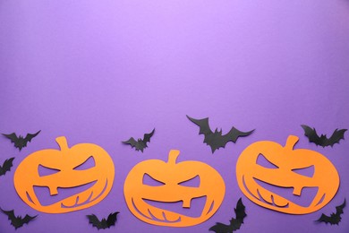 Photo of Flat lay composition with spooky paper pumpkins and bats on purple background, space for text. Halloween decor