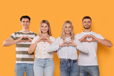 Happy volunteers making hearts with their hands on orange background