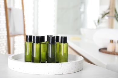 Mini bottles with cosmetic products on white table in bathroom. Space for text