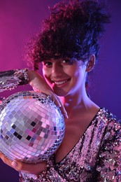 Beautiful young woman with disco ball posing on color background in neon lights
