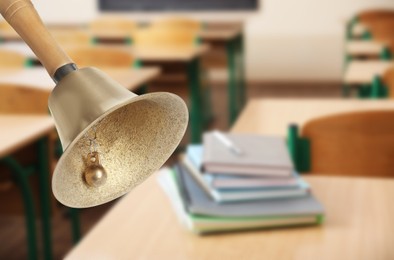 Image of Golden school bell with wooden handle and blurred view of books on desk in classroom