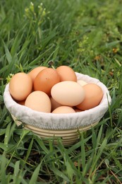 Fresh chicken eggs in basket on green grass outdoors