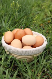 Photo of Fresh chicken eggs in basket on green grass outdoors