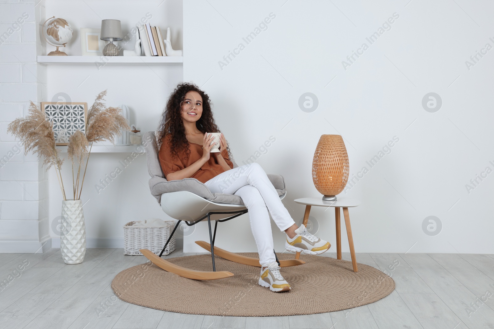 Photo of Young African-American woman with cup of drink sitting in rocking chair at home