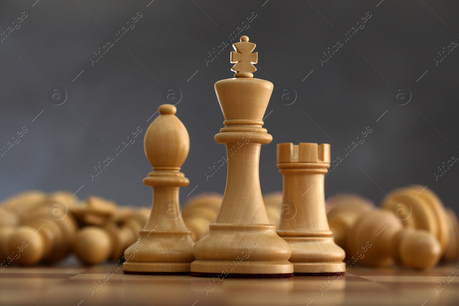 Photo of Wooden king, rook and bishop in front of fallen chess pieces on checkerboard against dark background, closeup