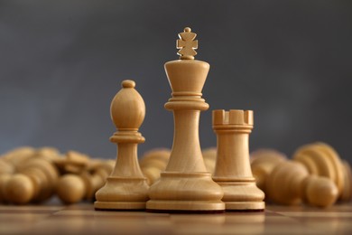 Photo of Wooden king, rook and bishop in front of fallen chess pieces on checkerboard against dark background, closeup