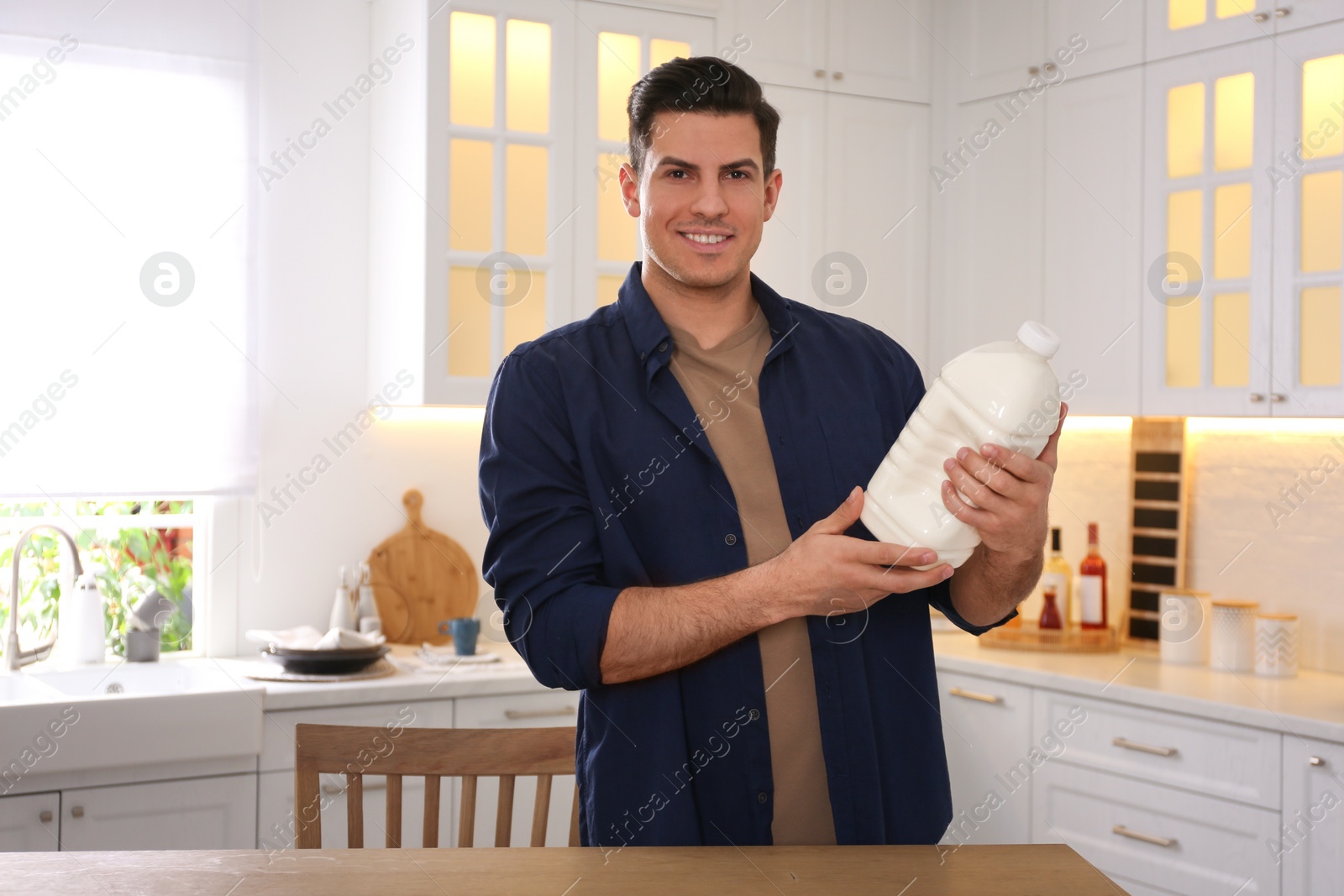 Photo of Man with gallon bottle of milk at wooden table in kitchen