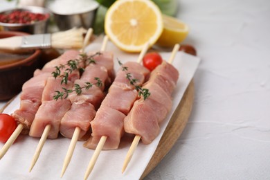 Skewers with cut raw meat, thyme and tomatoes on light textured table, closeup. Space for text