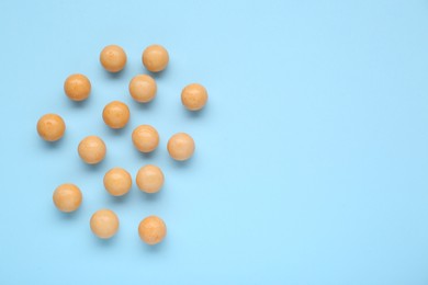 Many bright orange gumballs on light blue background, flat lay. Space for text