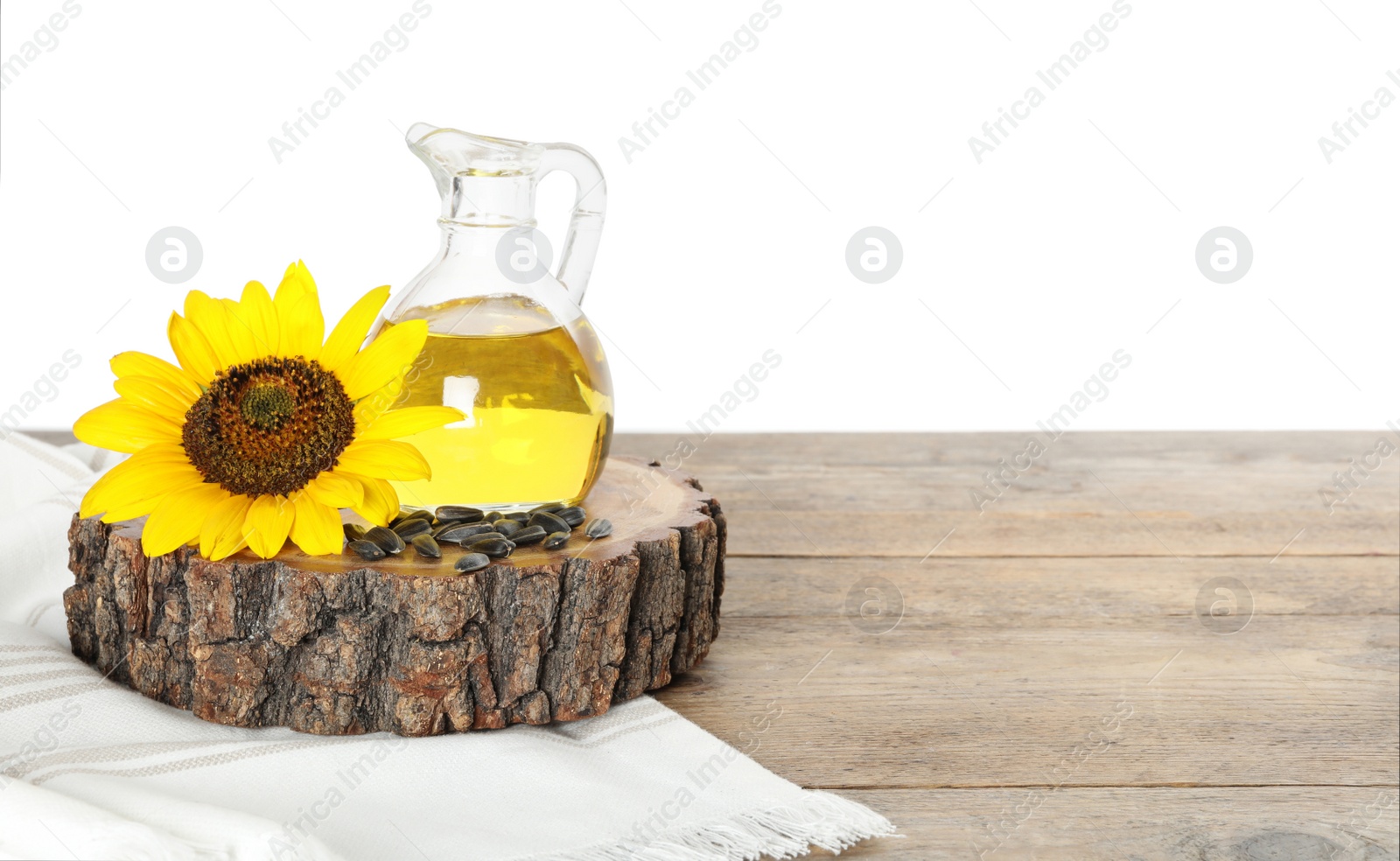 Photo of Sunflower, jug of oil and seeds on wooden table against white background, space for text