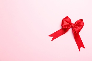 Red ribbon bow on color background, top view