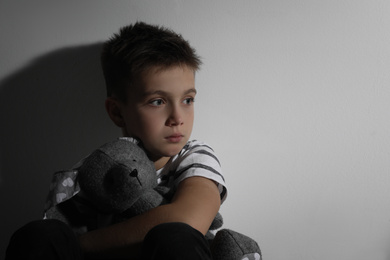 Photo of Sad little boy with toy near white wall, space for text. Domestic violence concept