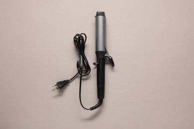 Curling iron on beige background, top view