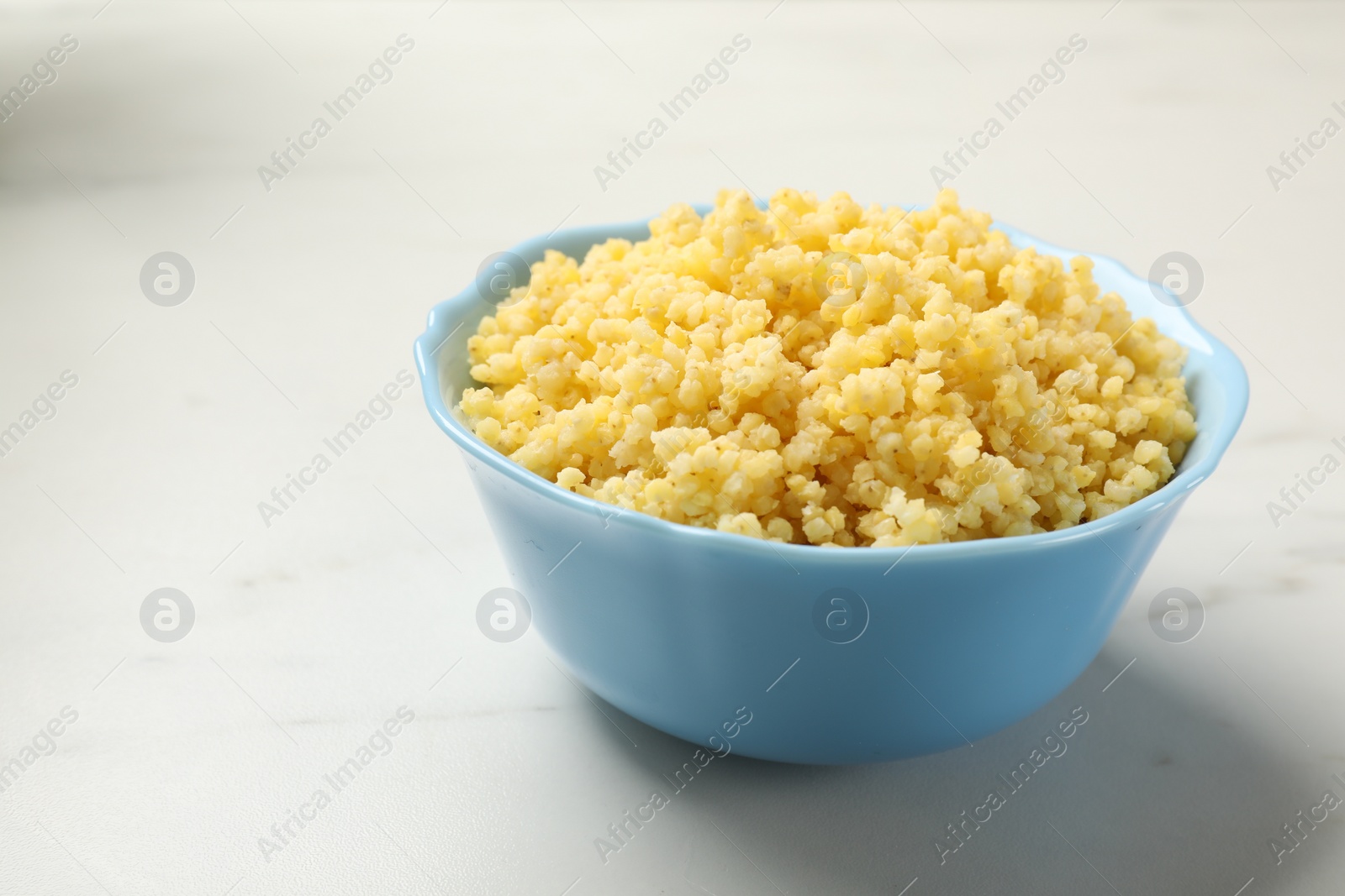 Photo of Tasty millet porridge in bowl on white marble table, closeup. Space for text