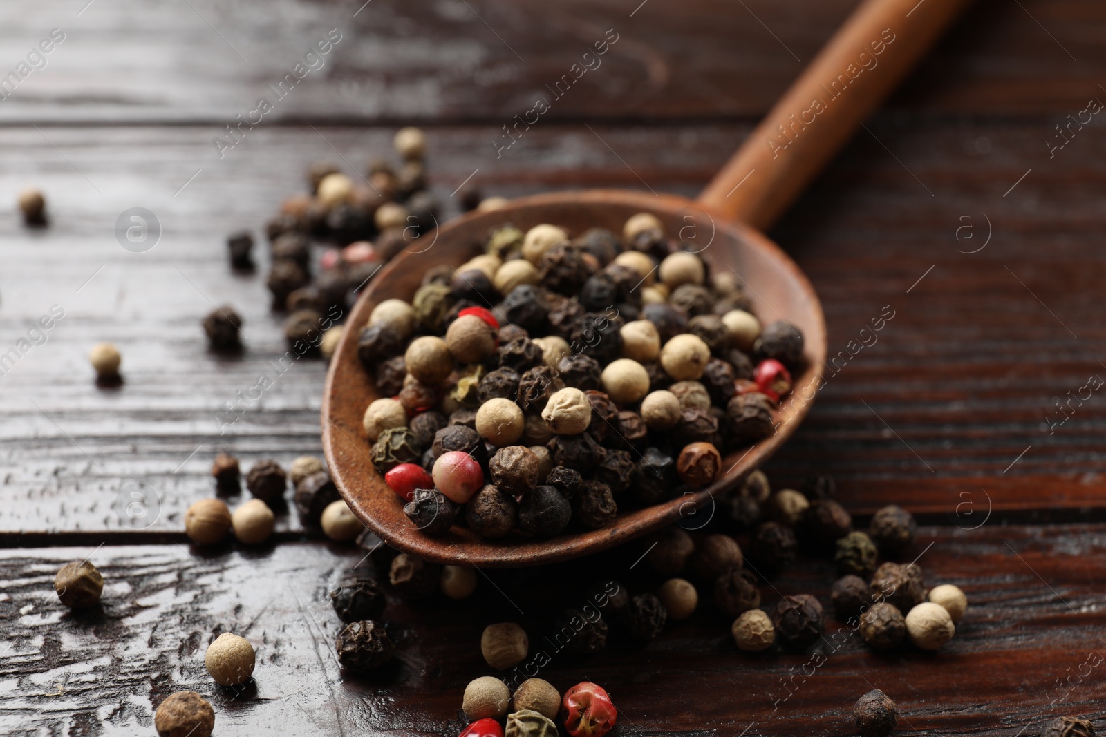 Photo of Aromatic spice. Different peppers in spoon on black table, closeup