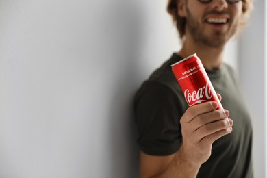 Photo of MYKOLAIV, UKRAINE - NOVEMBER 28, 2018: Young man with Coca-Cola can indoors, closeup. Space for text