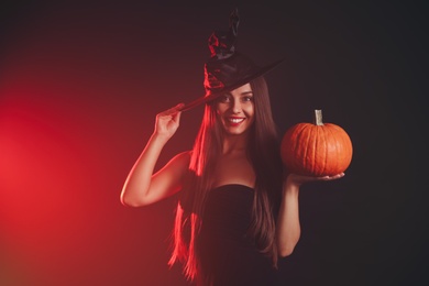 Photo of Young woman wearing witch costume with pumpkin on dark  background. Halloween party