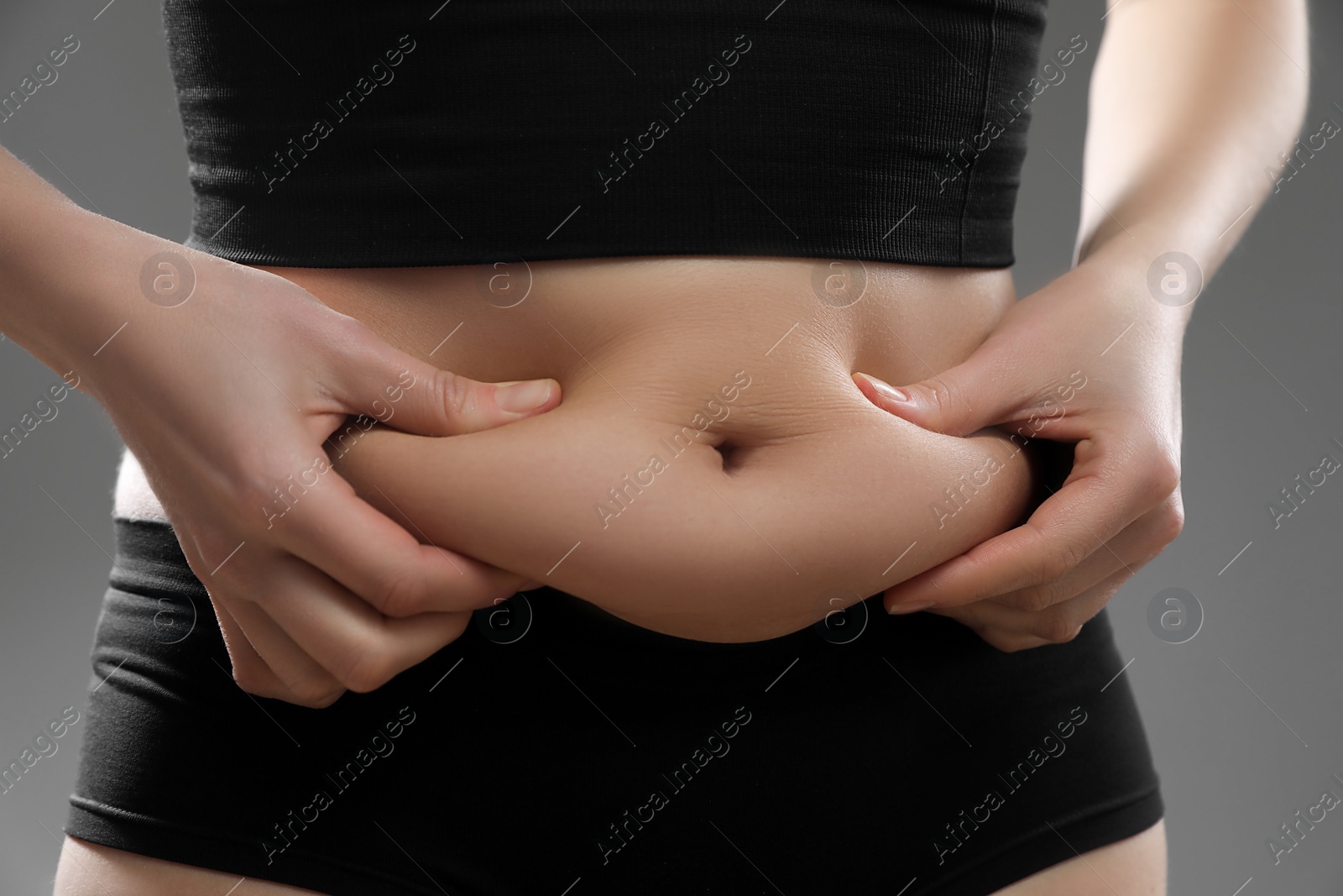 Photo of Woman touching belly fat on grey background, closeup. Overweight problem