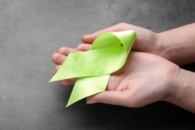 Photo of World Mental Health Day. Woman holding green ribbon on black background, closeup