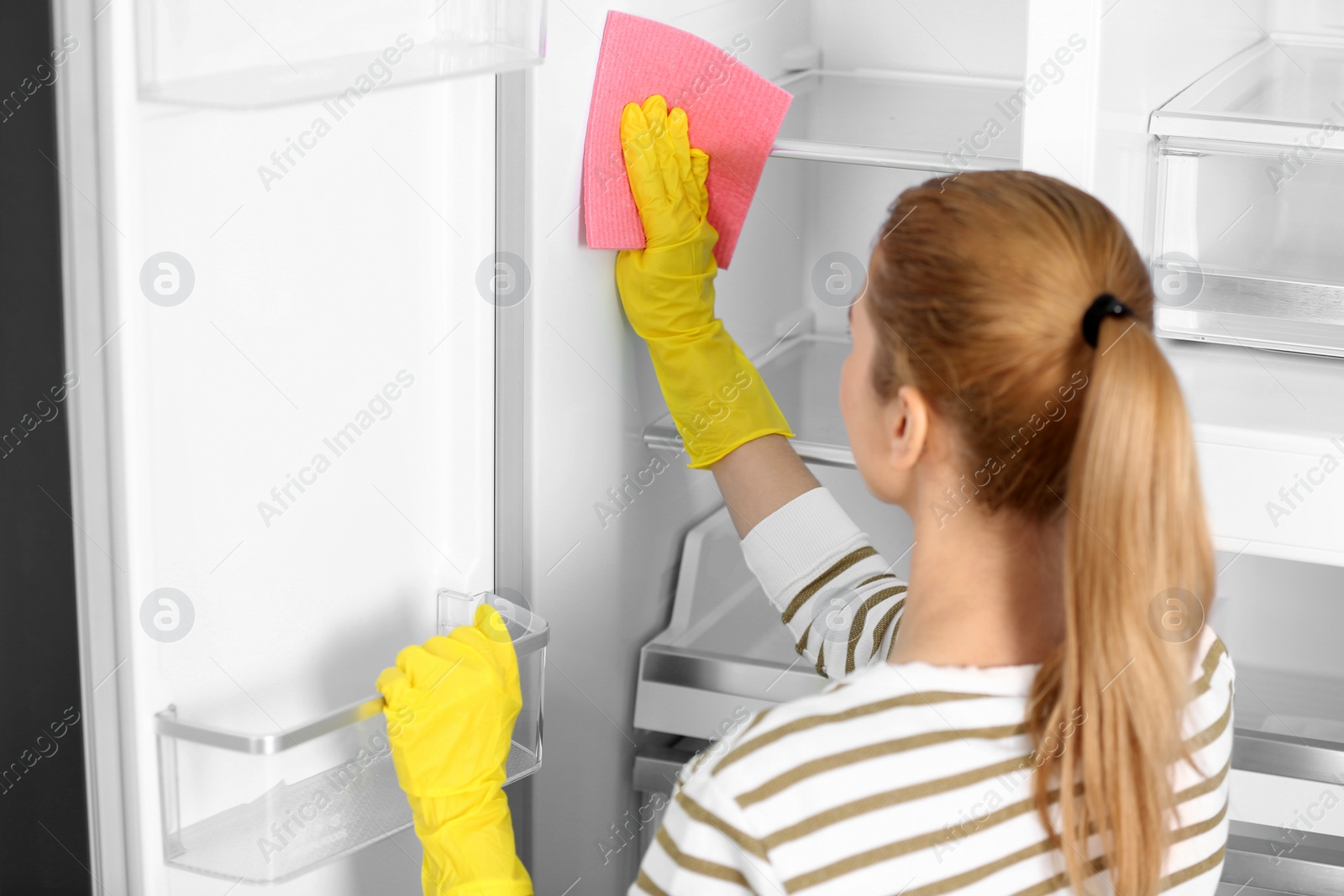 Photo of Woman in rubber gloves cleaning empty refrigerator at home