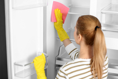 Woman in rubber gloves cleaning empty refrigerator at home