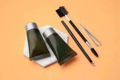 Photo of Eyebrow henna, professional tools and cosmetic products on orange background