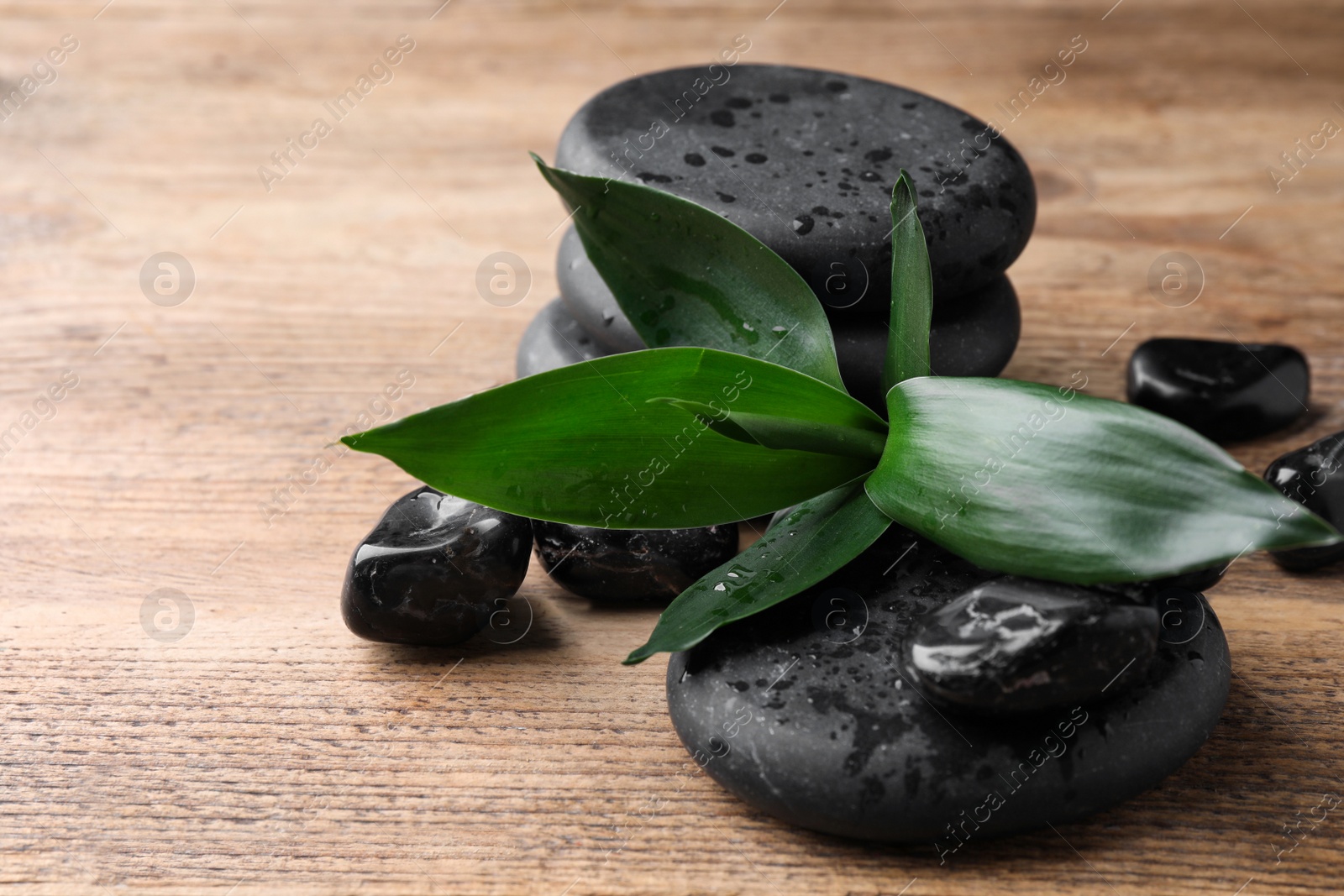 Photo of Wet spa stones and bamboo leaves on wooden table, closeup