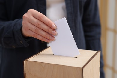 Photo of Woman putting her vote into ballot box on blurred background, closeup