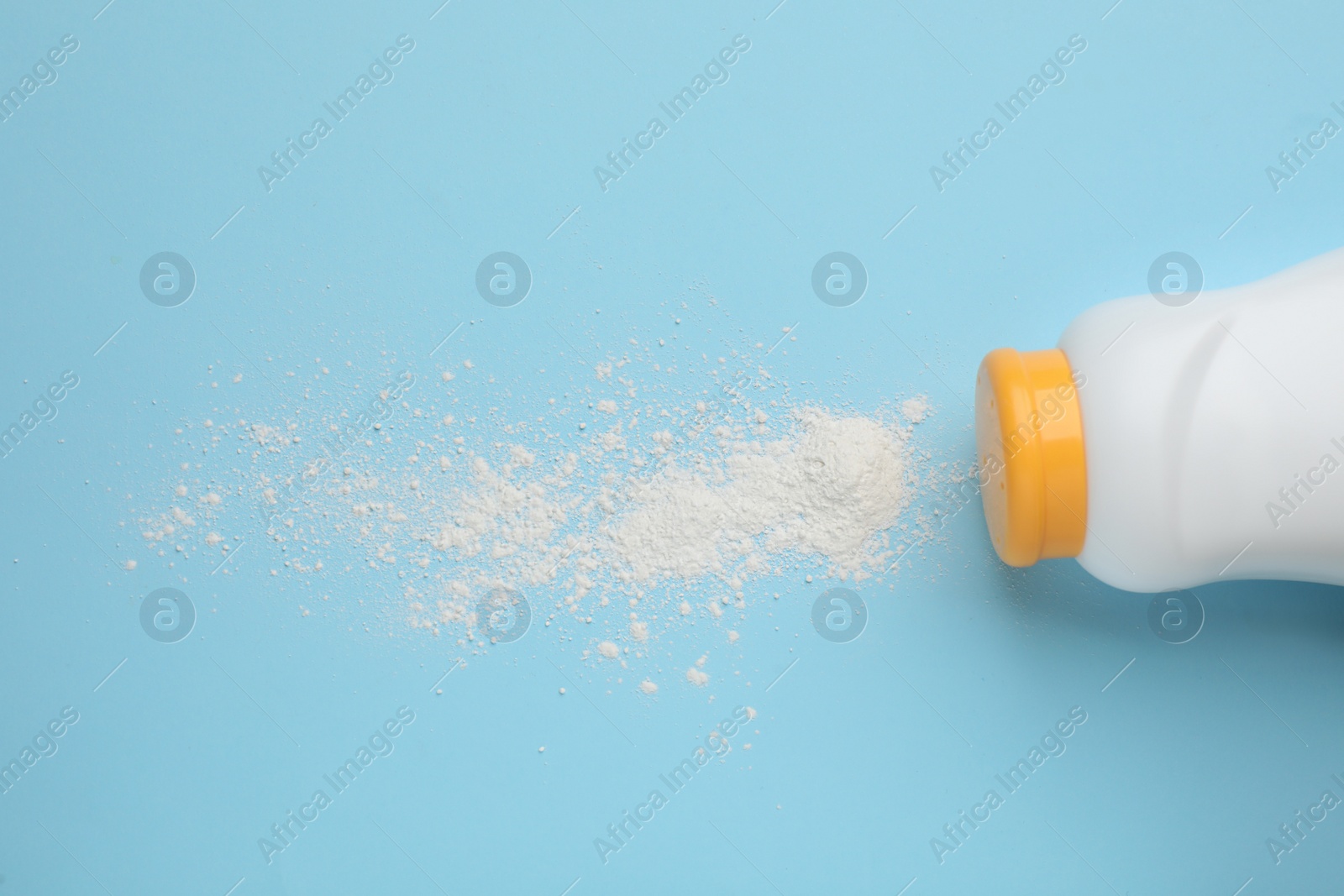 Photo of Bottle and scattered dusting powder on light blue background, top view. Baby cosmetic product