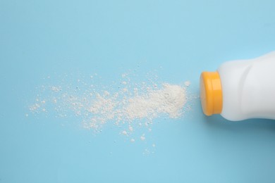 Bottle and scattered dusting powder on light blue background, top view. Baby cosmetic product