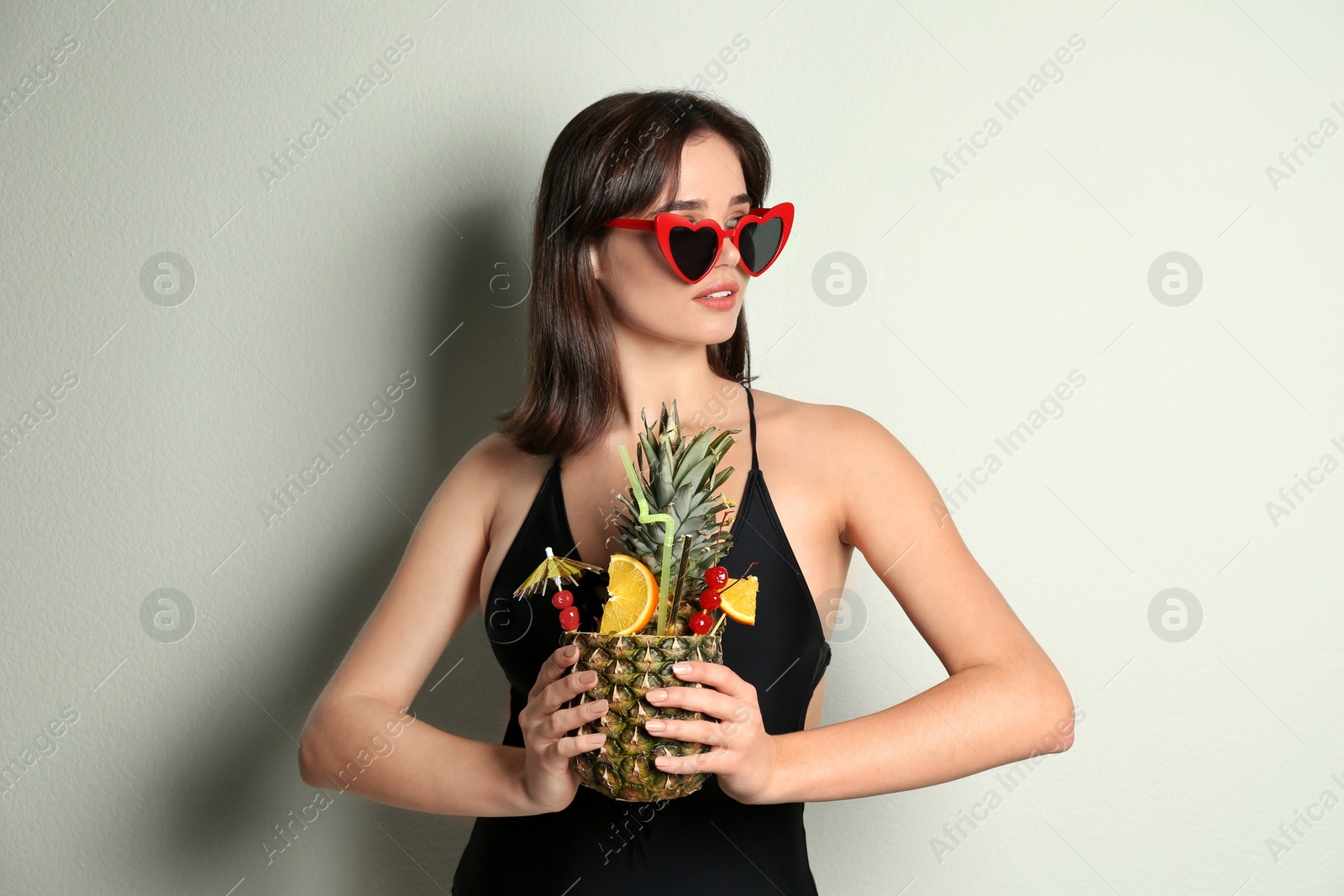 Photo of Beautiful woman in stylish swimsuit holding tropical cocktail on light grey background