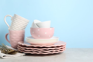 Beautiful ceramic dishware, cups and cutlery on light grey table, space for text