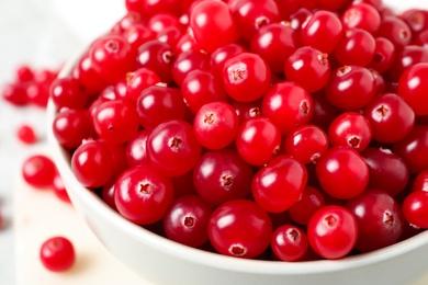 Photo of Bowl with tasty ripe cranberries on table, closeup