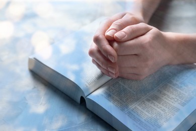 Image of Religion. Double exposure of sky and Christian woman praying over Bible at table, closeup. Bokeh effect