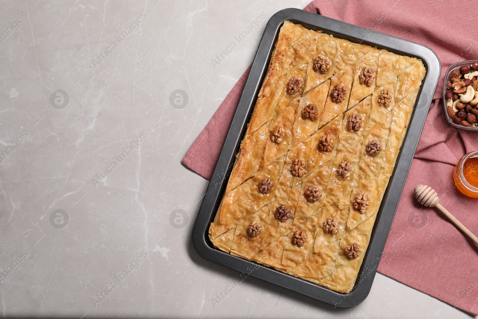 Photo of Delicious baklava with walnuts in baking pan, honey and nuts on grey table, flat lay. Space for text