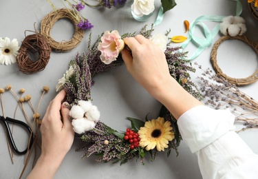 Photo of Florist making beautiful autumnal wreath with heather flowers at light grey table, top view
