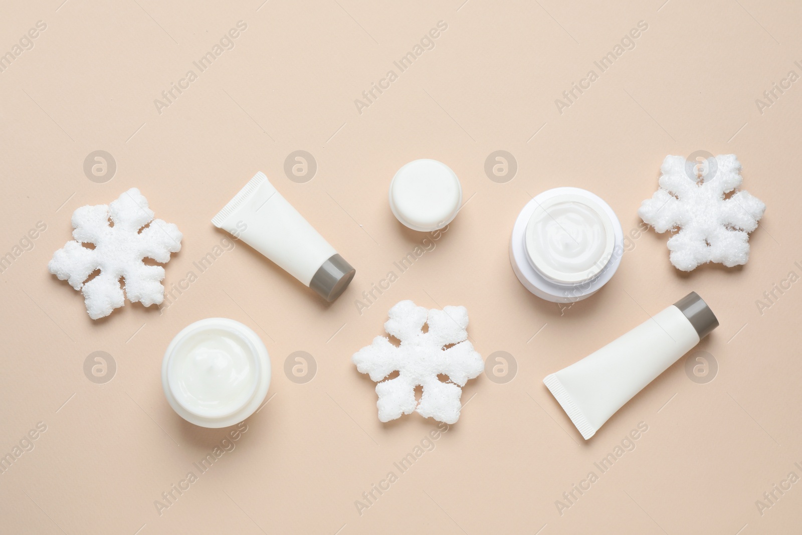 Photo of Flat lay composition with cosmetic products and snowflakes on beige background. Winter skin care