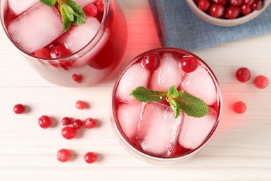 Tasty cranberry juice with ice cubes in glasses and fresh berries on white wooden table, flat lay