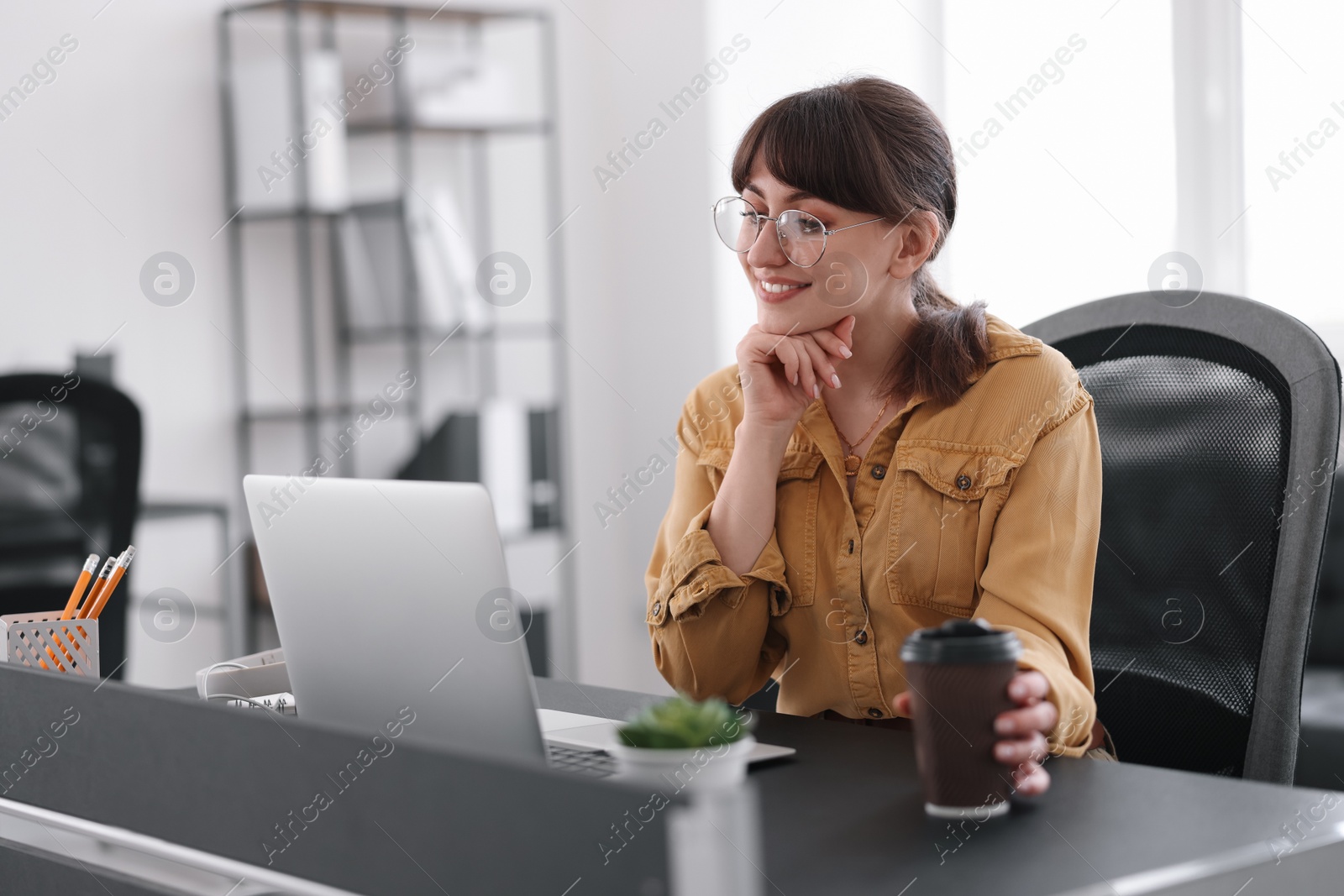 Photo of Woman with cup of coffee watching webinar at table in office